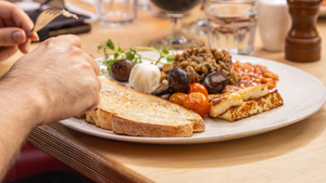 Plate of food with toast, vegetables, and a hand holding a fork on a wooden table.