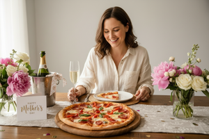 Woman sitting at a table with pizza and flowers, celebrating Mother's Day.