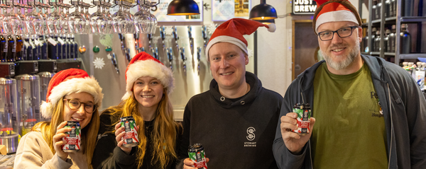 Four people wearing Santa hats holding drinks in a bar setting.